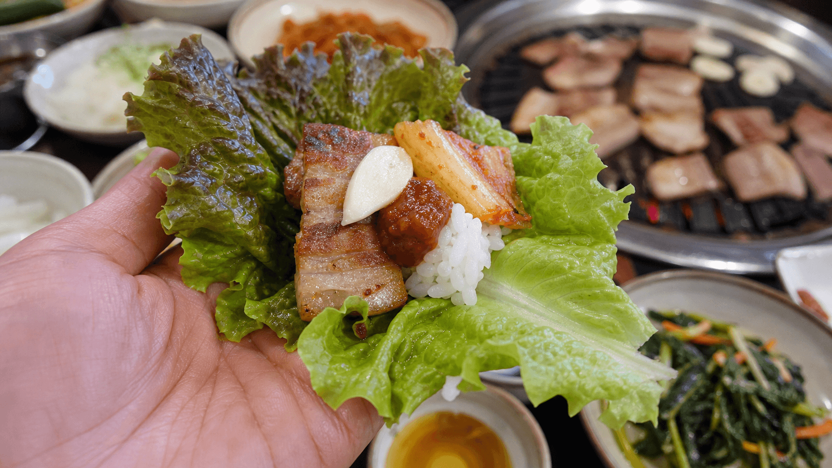A Korean barbecue lettuce wrap with grilled pork belly, ssamjang, garlic, kimchi and rice